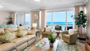 A spacious living room with a beige sofa, two armchairs, a coffee table, and a view of the ocean through large windows. - Hidden Dunes 402 (Panama City Beach)