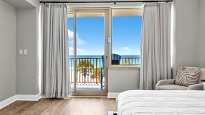 Ein Schlafzimmer mit einem großen Bett, einem Balkon mit Blick auf den Strand und einer Schiebetür.