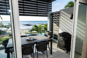 Enjoy al fresco dining with a view of the beach from this outdoor dining area, featuring a table, teapot, cups, and grill.