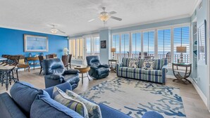 A spacious living room with a blue wall, a large window, and a ceiling fan. - Hidden Dunes 1704 (Panama City Beach)