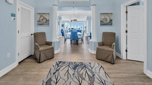 A hallway with two armchairs, a dining area with a blue table and chairs, and a view into a kitchen. - Hidden Dunes 1704 (Panama City Beach)