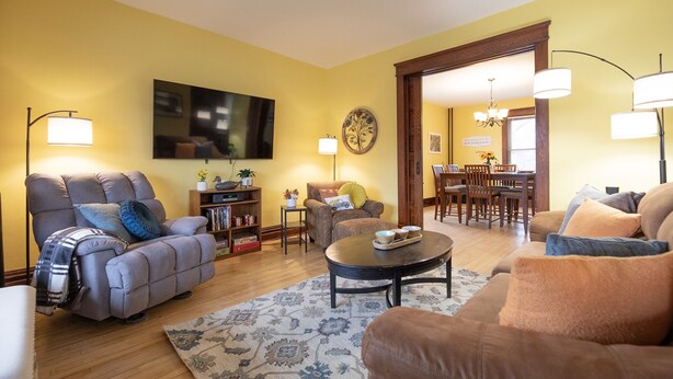 A living room with a sofa, armchairs, a coffee table, and a TV mounted on the wall. - Historic Hammond Home- Close to Duluth! Game Room & Pet Friendly: Dogs & Cats! (Superior)
