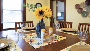 A dining table set with a floral table runner, a vase with yellow flowers, and a candle holder with a candle. - Historic Hammond Home- Close to Duluth! Game Room & Pet Friendly: Dogs & Cats! (Superior)