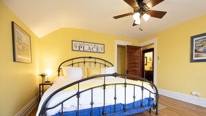 A bedroom with a metal bed frame, wooden flooring, a ceiling fan, and a 'Welcome to Our Place' sign. - Historic Hammond Home- Close to Duluth! Game Room & Pet Friendly: Dogs & Cats! (Superior)