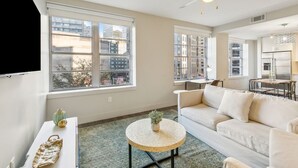 Ein modernes Wohnzimmer mit einem weißen Sofa, einem runden Couchtisch und einem großen Fenster mit Blick auf die Stadt.