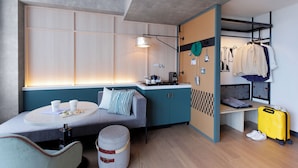 A compact hotel room with a kitchenette, a seating area with a table and chairs, a bench, a bed with a checkered headboard, and a luggage rack. - Caption by Hyatt Namba Osaka (Osaka)