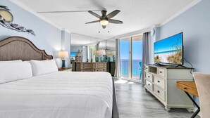 A bedroom with a large bed, a ceiling fan, a TV, and a view of the ocean through a balcony. - Dunes of Panama 2002e (Panama City Beach)