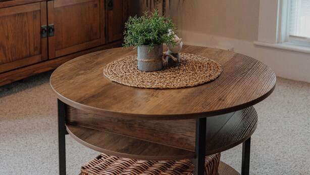 Une table ronde en bois, surmontée d’un set de table en fibres tressées, un panier en osier et une petite plante en pot.