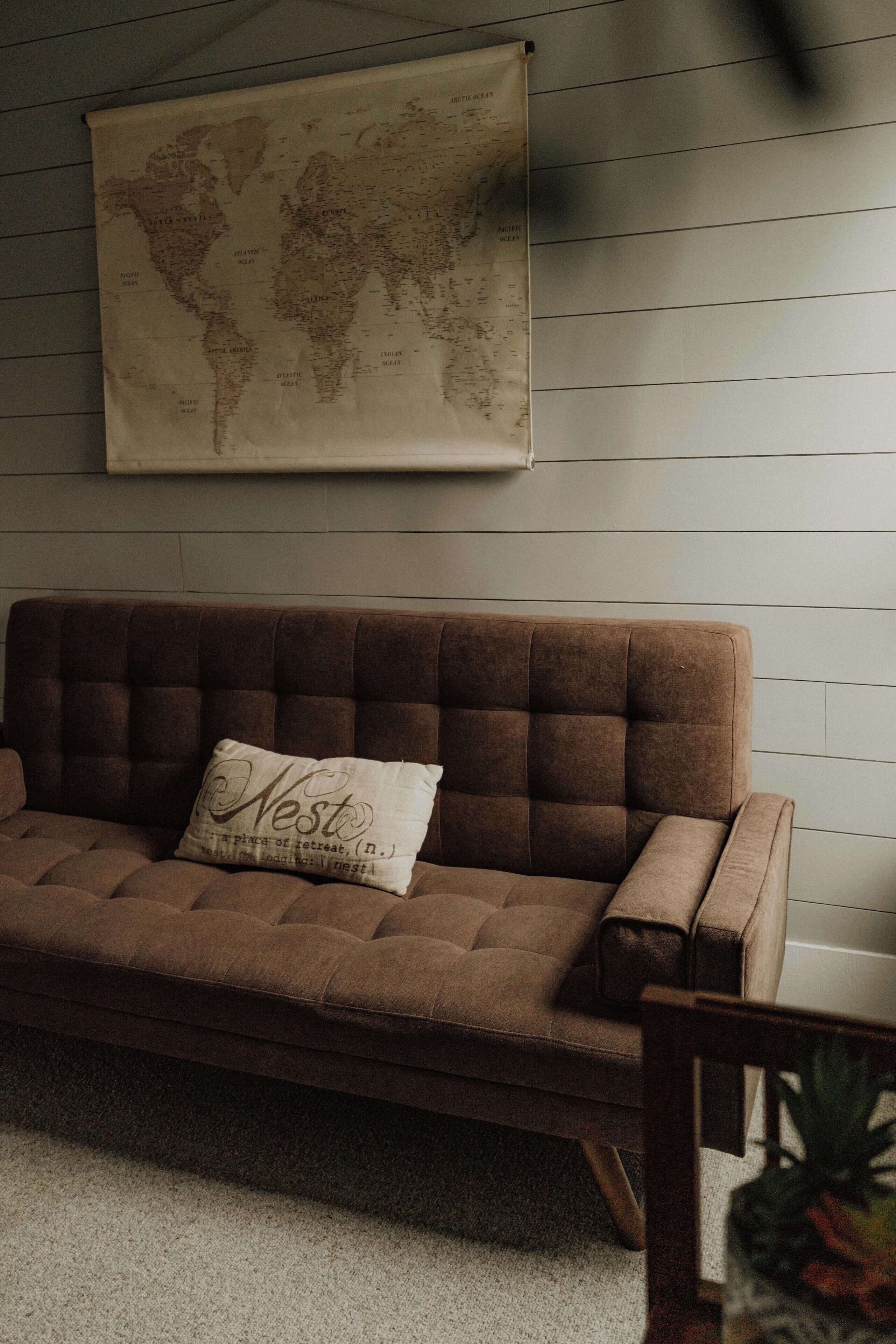 A brown sofa with a cushion labeled "Nest" against a wall with a world map.