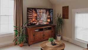 Un salon chaleureux avec un grand téléviseur à écran plat, un meuble en bois, une table basse ronde et une plante en pot.