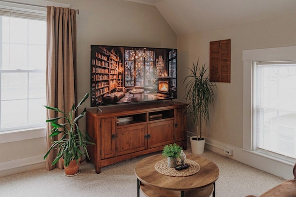 A cozy living room with a large flat-screen TV, a wooden cabinet, a round coffee table, and a potted plant.