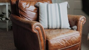 Un fauteuil en cuir marron avec un coussin à rayures, une horloge murale et une plante en pot.