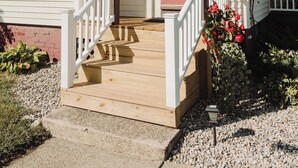 Une maison à deux étages avec un porche à l’avant, une porte rouge et un petit jardin agrémenté de fleurs rouges.