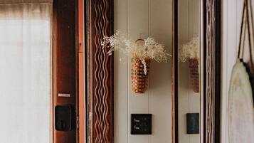 A wooden door with a mirror, a small basket with dried flowers, and a light switch on the wall.