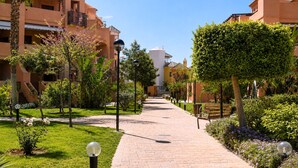 Un sendero pavimentado bordeado de vegetación y edificios con balcones, que conduce a un edificio central blanco.