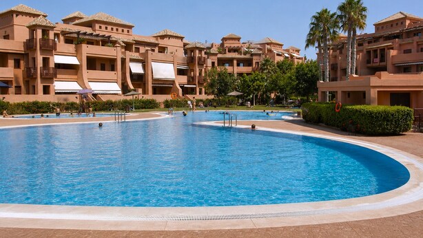 Una gran piscina rodeada de edificios de varios pisos con balcones y palmeras.