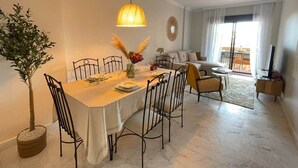 Un comedor con una mesa dispuesta para seis personas, rodeada de sillas, una planta en maceta y una lámpara colgante.