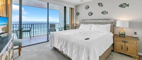 A bedroom with a large bed, a nightstand, a chair, and a view of the ocean.