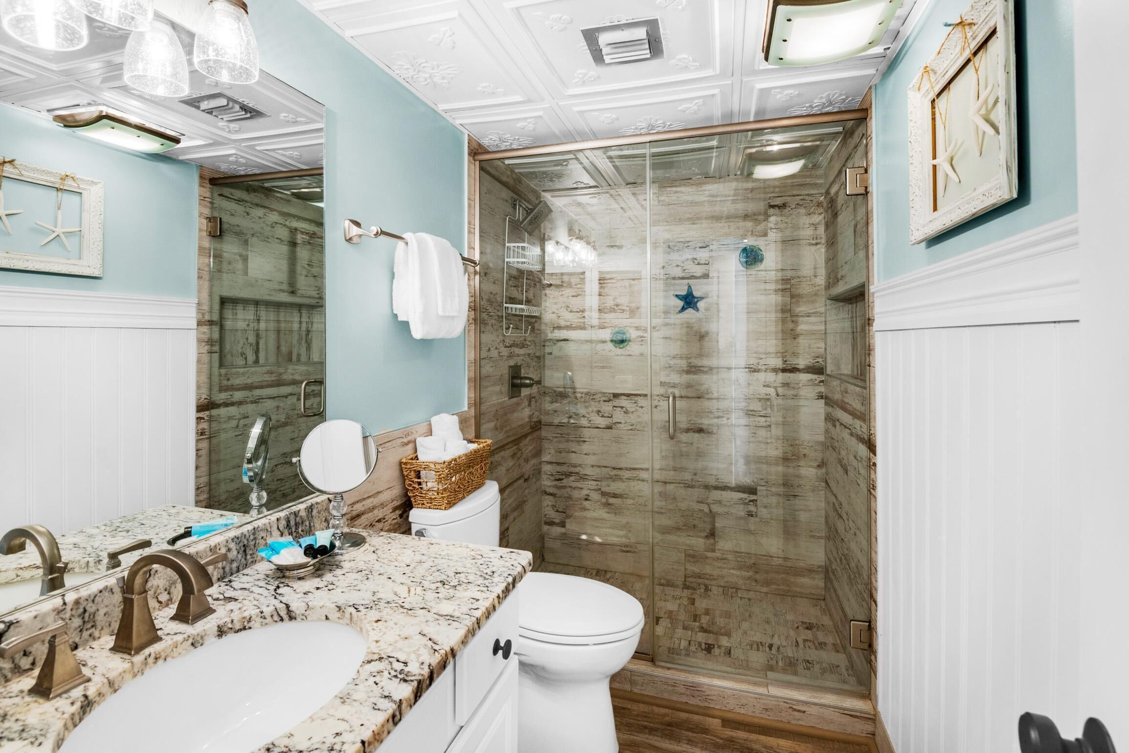 Un baño con lavamanos de mármol, inodoro blanco, cabina de ducha de vidrio y pared de madera.