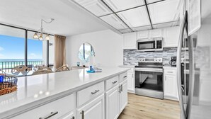 A modern kitchen with white cabinets, a large island, stainless steel appliances, and a view of the ocean.