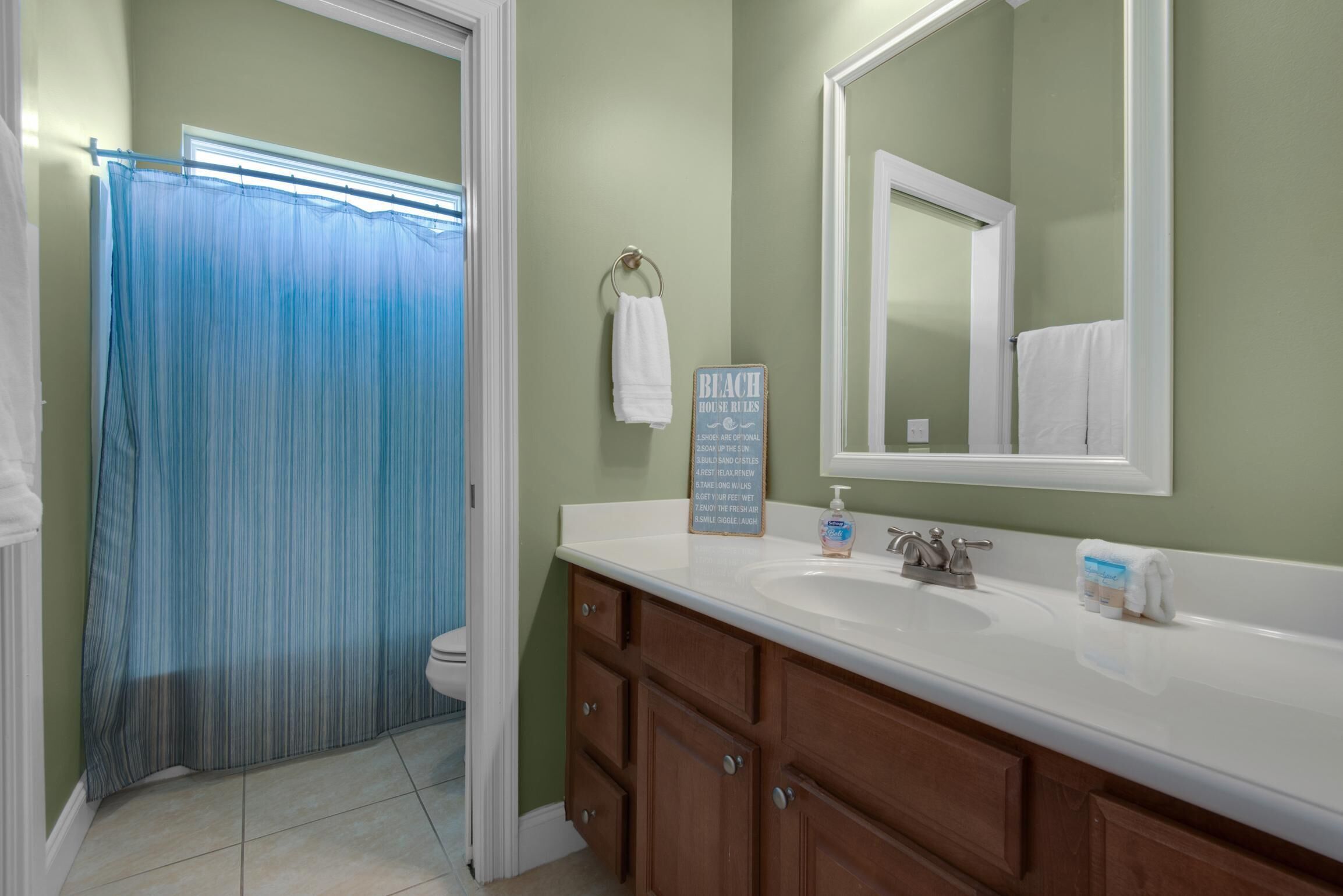 A bathroom with a shower curtain, a sink with a soap dispenser, and a towel rack.
