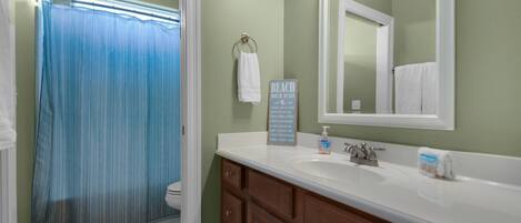 A bathroom with a shower curtain, a sink with a soap dispenser, and a towel rack.