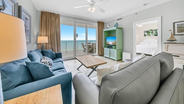 Ein modernes Wohnzimmer mit einer Couch, einem Couchtisch und einer TV-Konsole. Es gibt einen Balkon mit Meerblick.