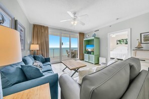 A modern living room with a sofa, a coffee table, and a TV stand. There is a balcony with a view of the ocean. - Twin Palms 804 (Panama City Beach)