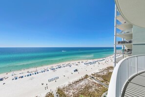 Uitzicht op het strand vanaf een hotelbalkon, met een heldere lucht, zandstrand en een kalme zee.