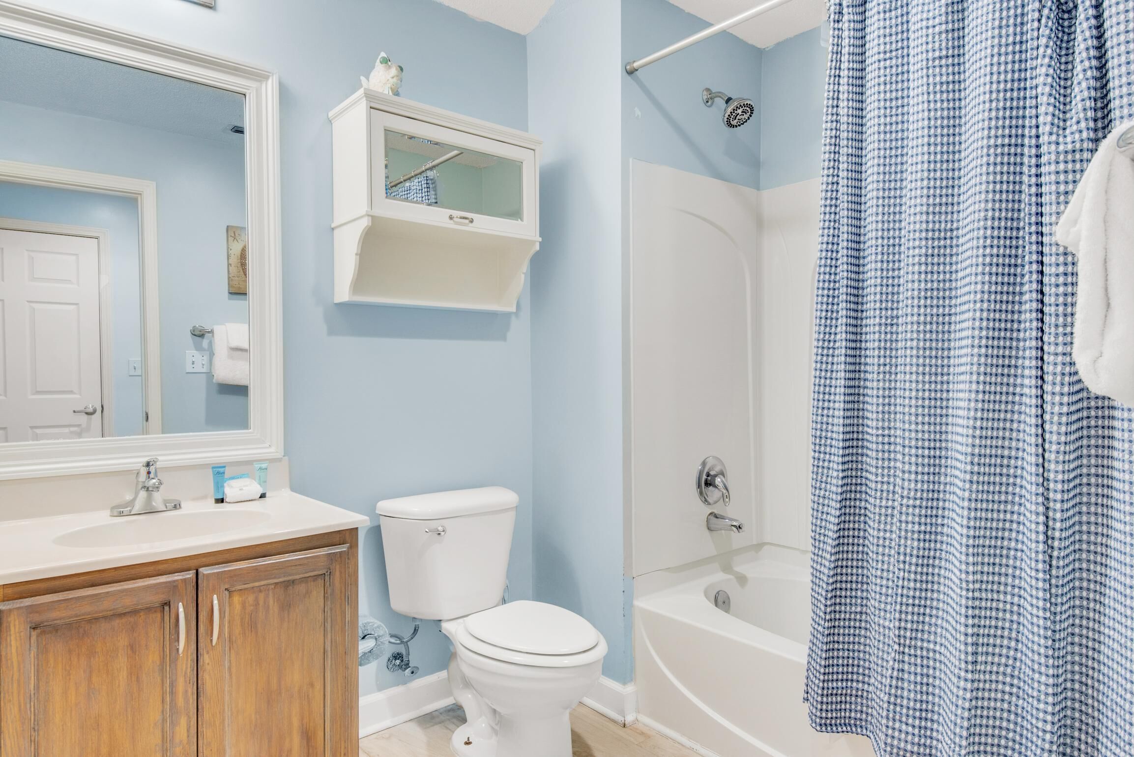 A bathroom with a white sink, wooden cabinets, a toilet, a white bathtub, and a blue checkered shower curtain.