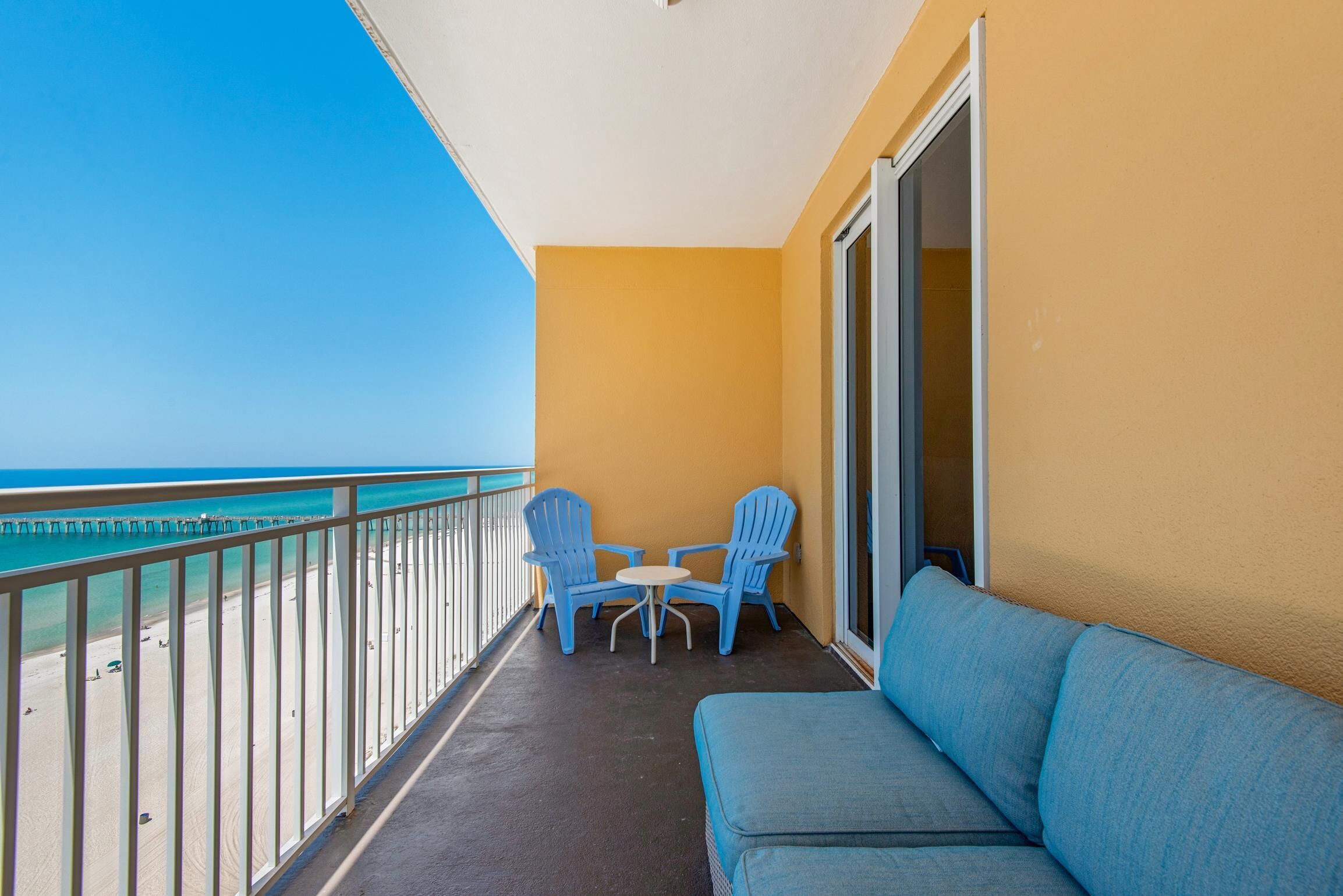 A balcony with a sofa and two chairs, overlooking a beach.