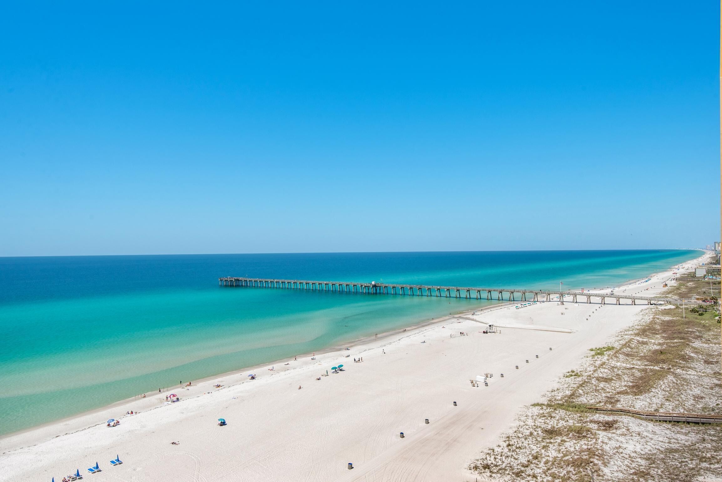 Ein Strand mit einem Steg, der sich ins Meer erstreckt, feinem Sand und klarem, blauem Wasser.