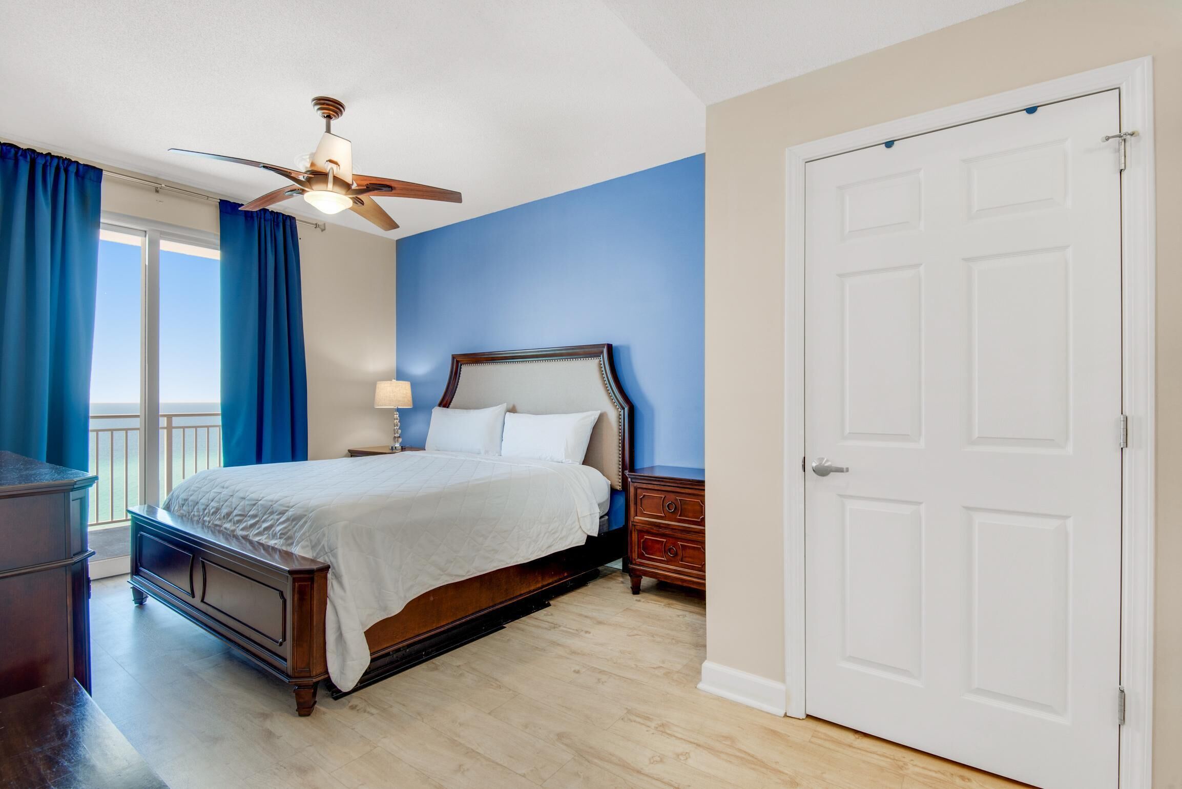 A bedroom with a bed, a nightstand, a dresser, a ceiling fan, and a white door.