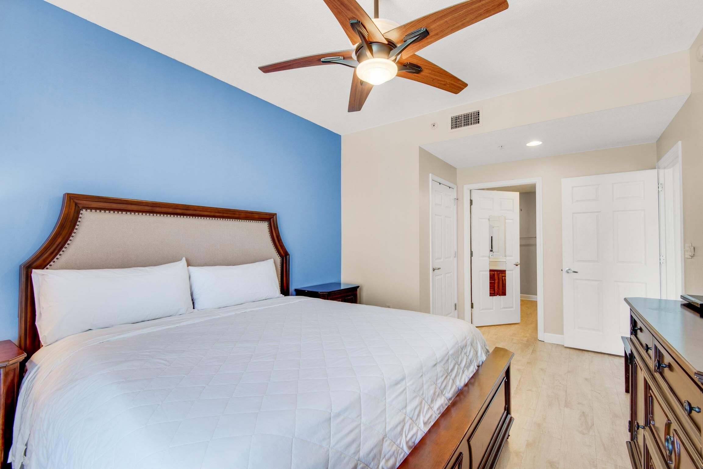 A bedroom with a large bed, wooden headboard, a ceiling fan, and white walls.