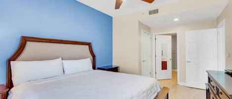 A bedroom with a large bed, wooden headboard, a ceiling fan, and white walls.