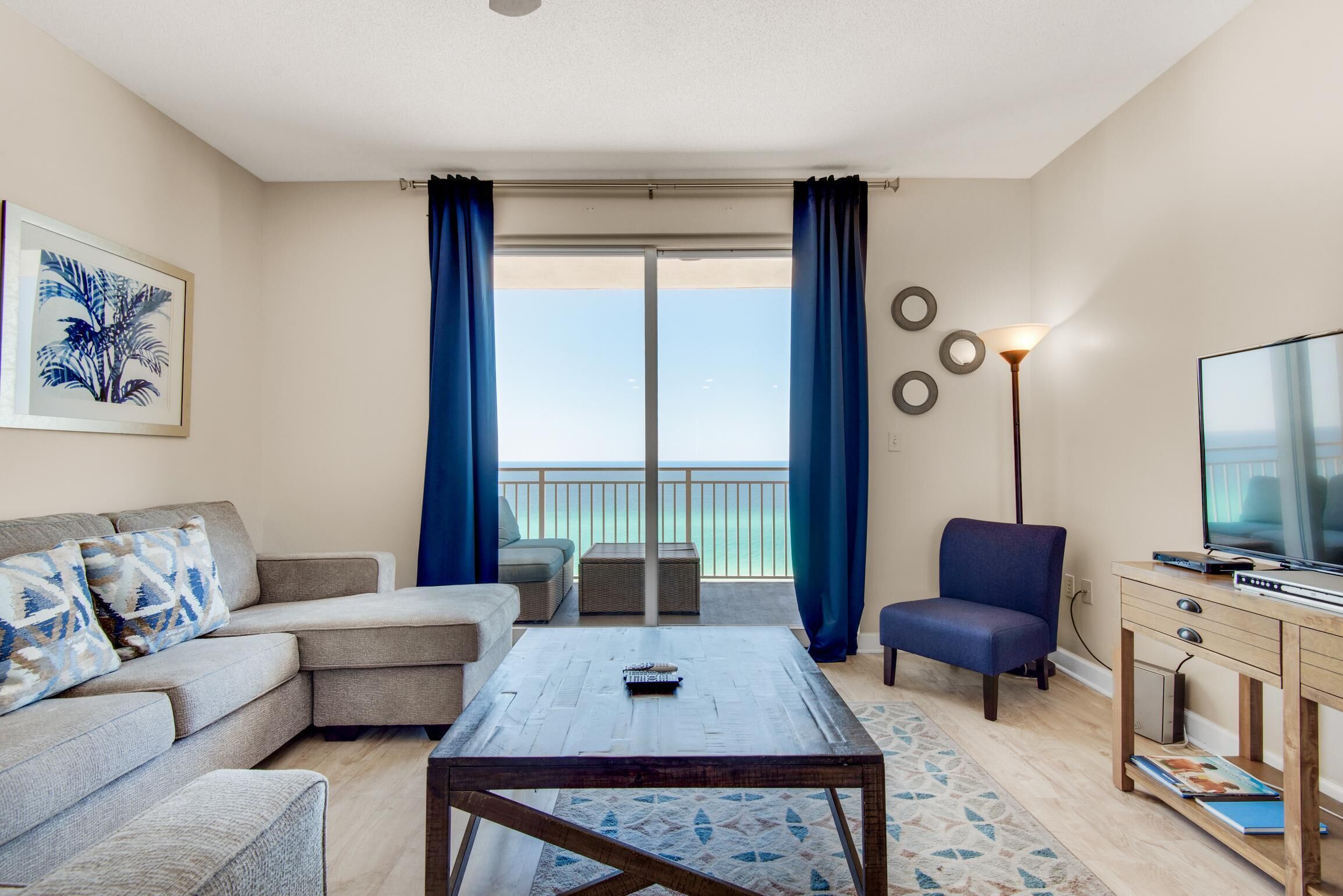 A living room with a sofa, a coffee table, a TV, and a balcony with curtains.