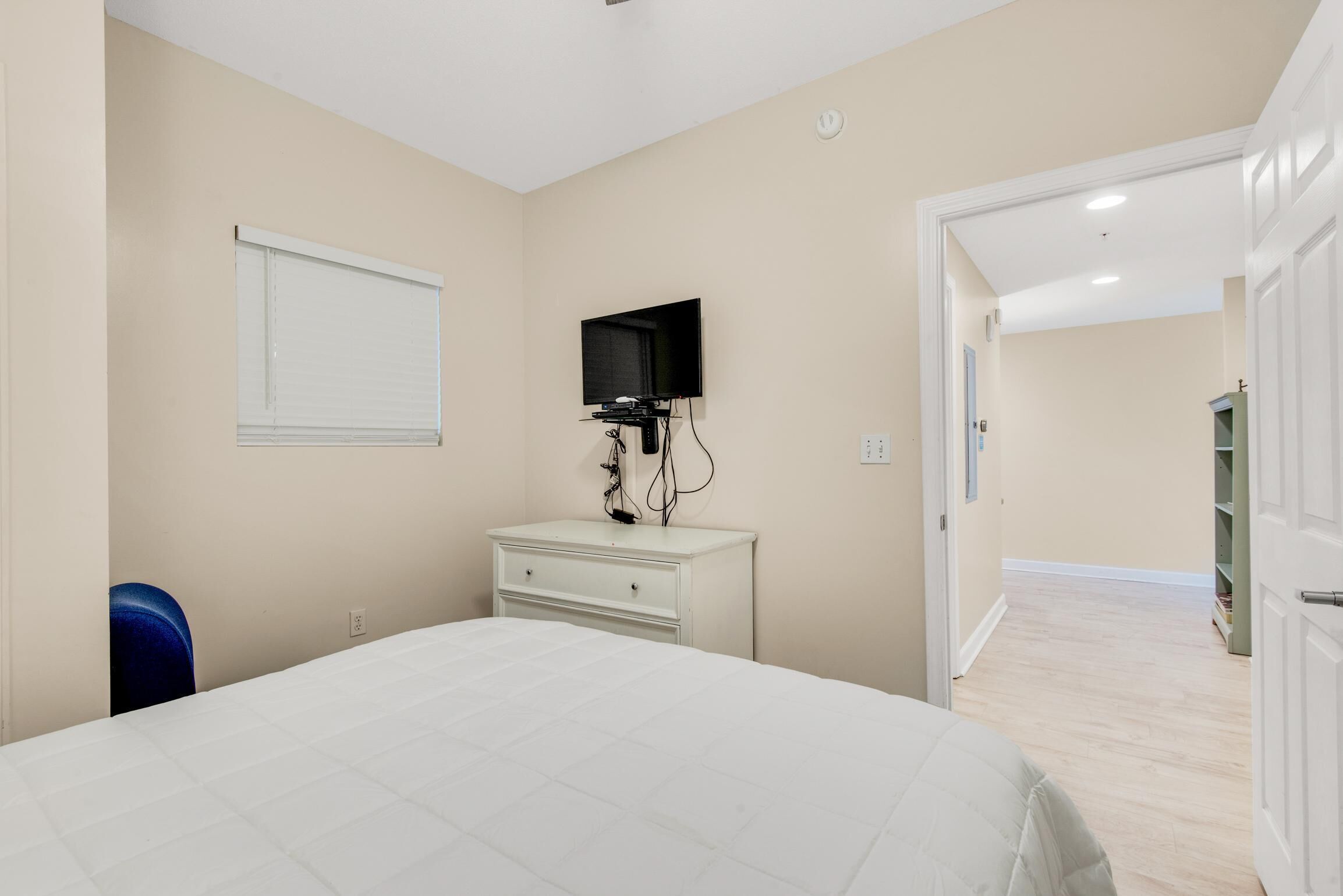 A bedroom with a bed, a dresser, a television, and a window with blinds.