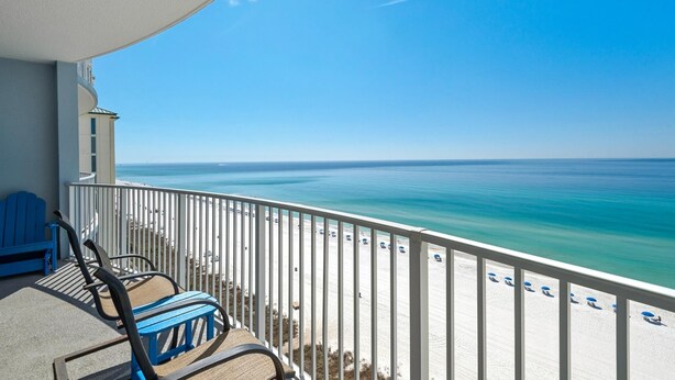 Een balkon met uitzicht op de oceaan, een wit hekwerk en blauwe stoelen.
