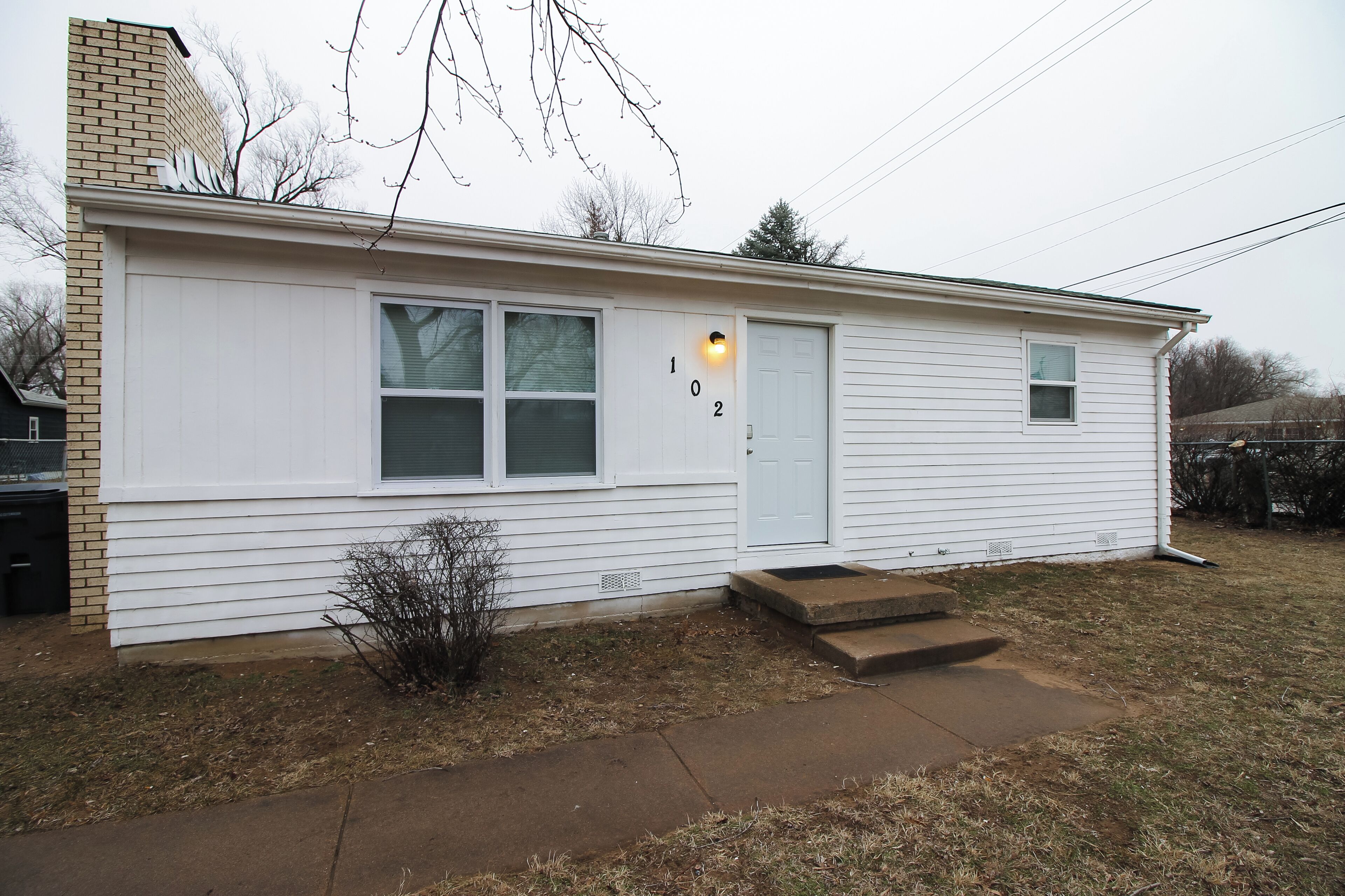 A single-story house with a white exterior, a front door, and a small front yard.