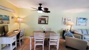 A dining area with a wooden table and chairs, a ceiling fan, and a kitchen visible through a mirror. - Rockin Robin-gulf Highlands 151 (Panama City Beach)