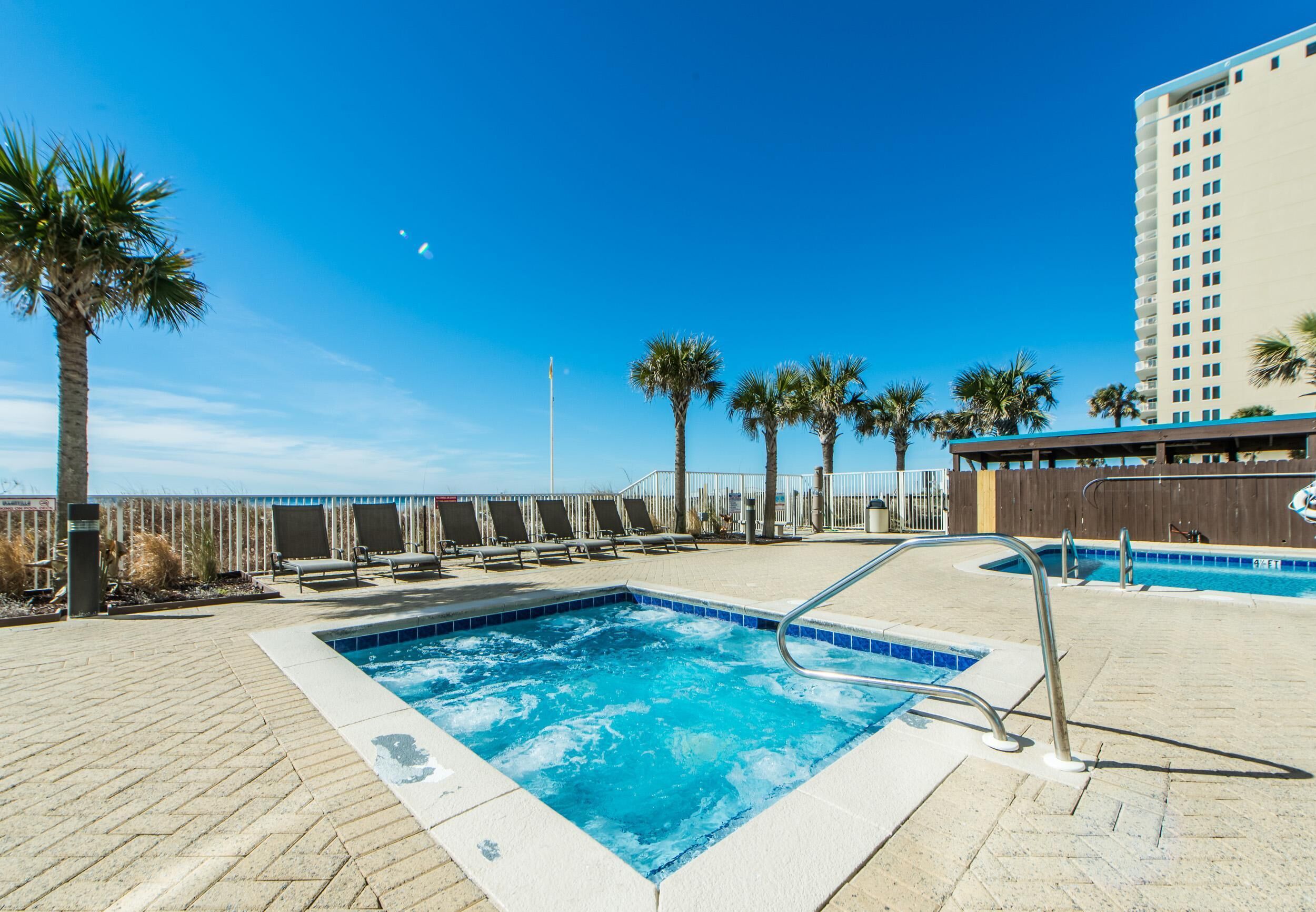 Un área de piscina en la azotea con sillones de descanso, palmeras y vista al océano.