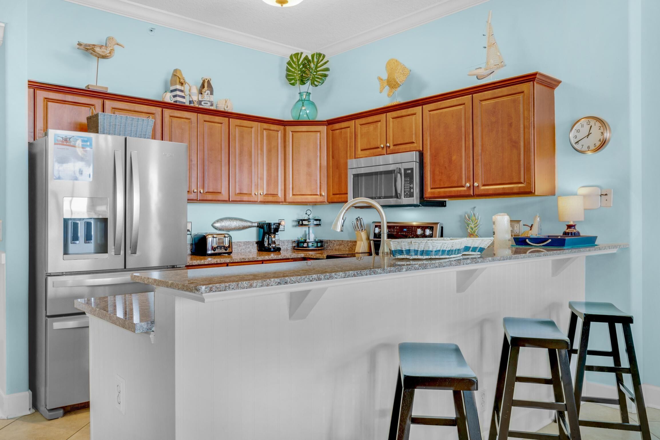 A kitchen with wooden cabinets, stainless steel appliances, a large island with stools, and decorative items on the walls.