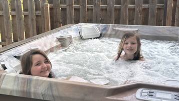 Een hottub met twee personen erin, omgeven door een houten omheining en een huis op de achtergrond.