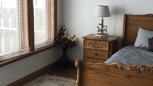 Ein Schlafzimmer mit einem hölzernen Bett, einem Nachttisch mit Lampe und einem Fenster mit Jalousien.