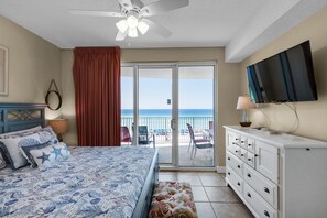 A bedroom with a bed, a dresser, a television, and a view of the ocean through a sliding glass door.