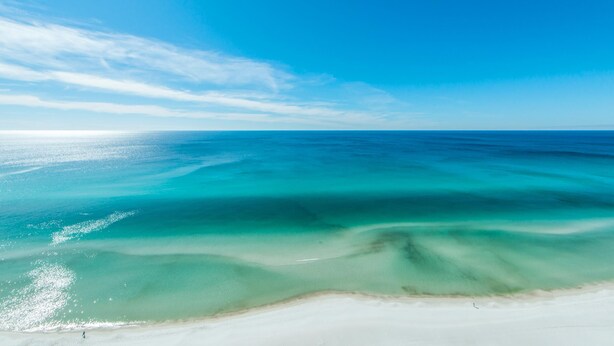 Une plage aux eaux turquoise et limpides, bordée d’un rivage sablonneux.