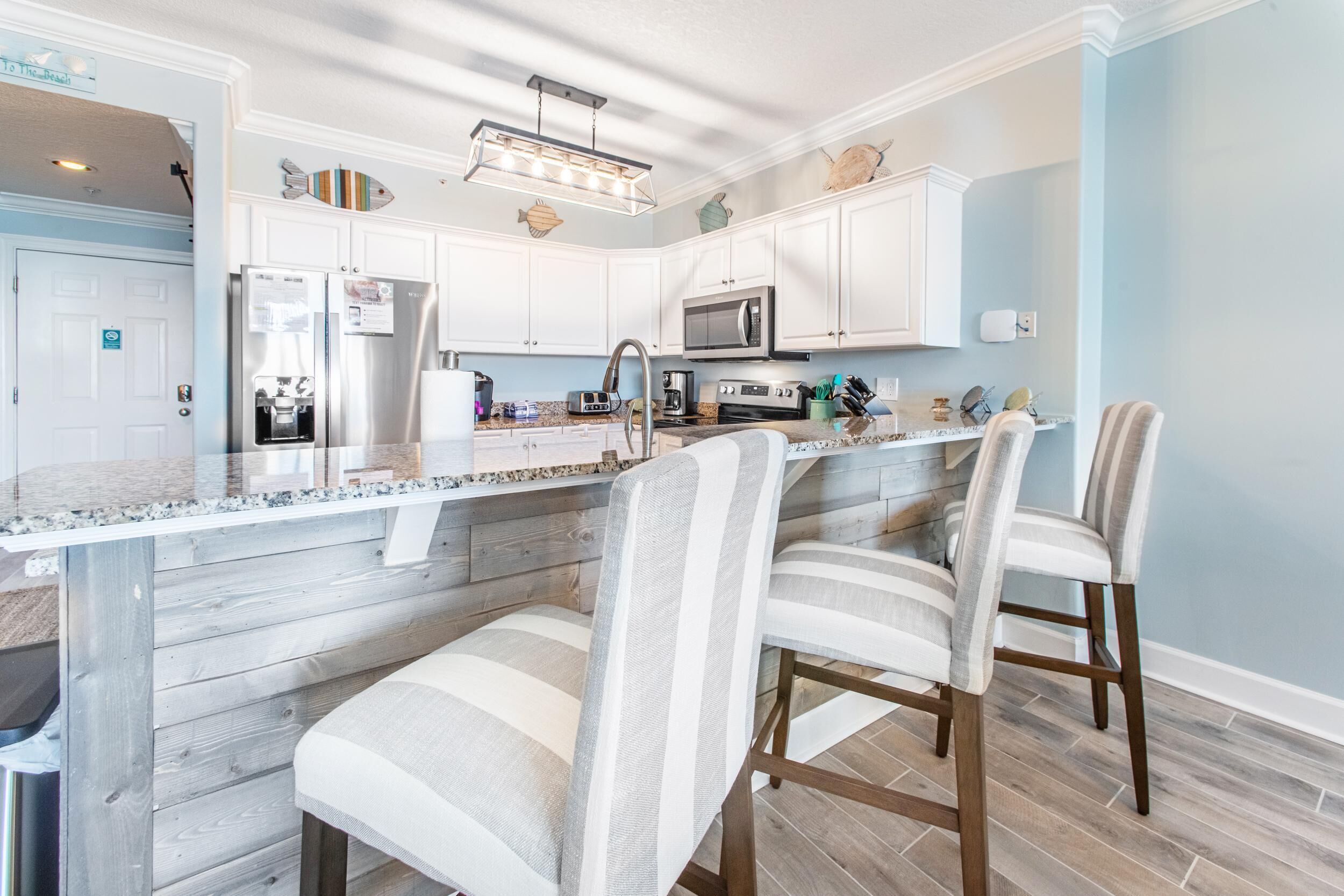 A modern kitchen with white cabinets, stainless steel appliances, and a granite countertop. There are three striped chairs at the island.
