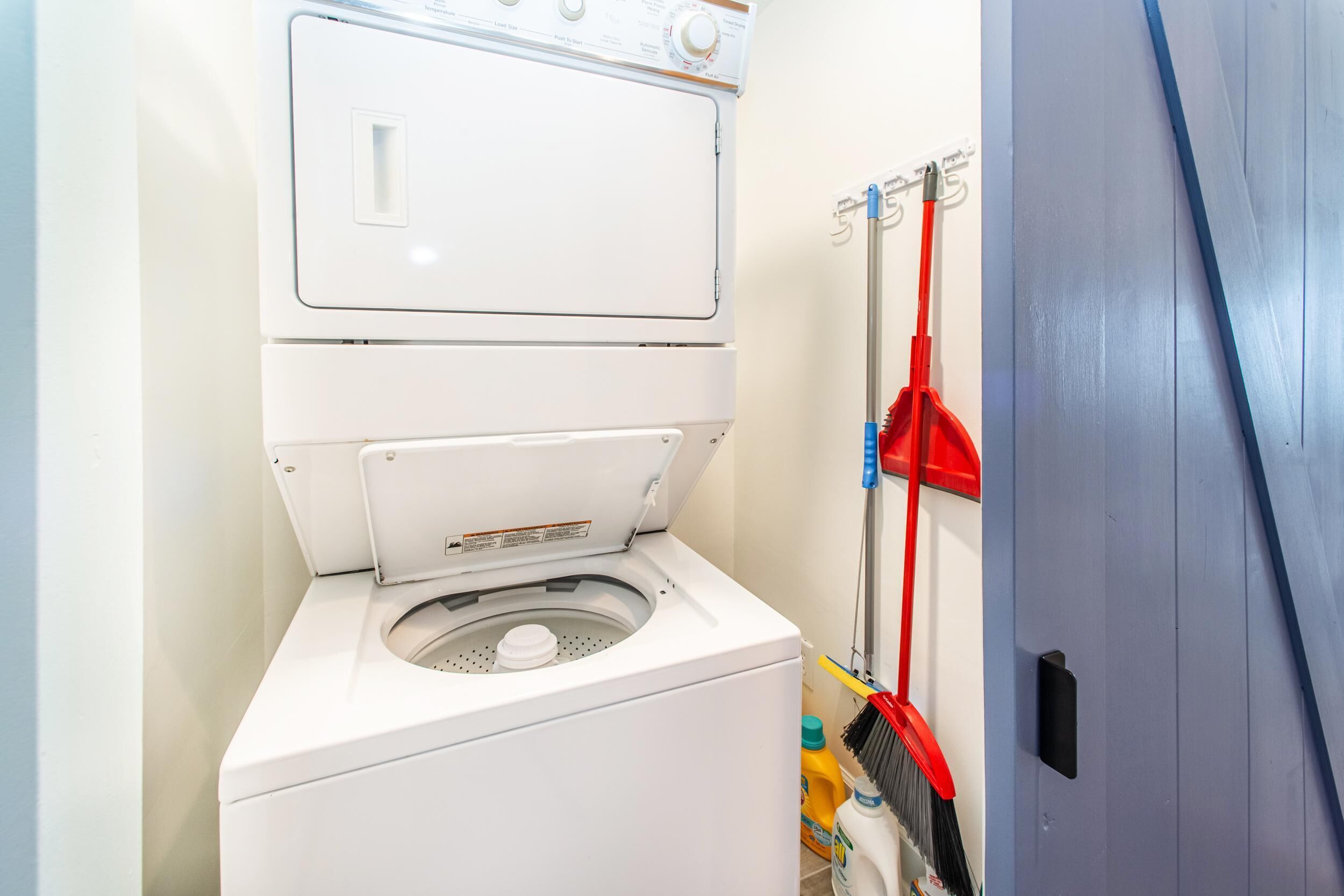 Un espace réduit dédié à la buanderie, comprenant un lave-linge et un sèche-linge à chargement frontal, un balai-mop et des produits de nettoyage.