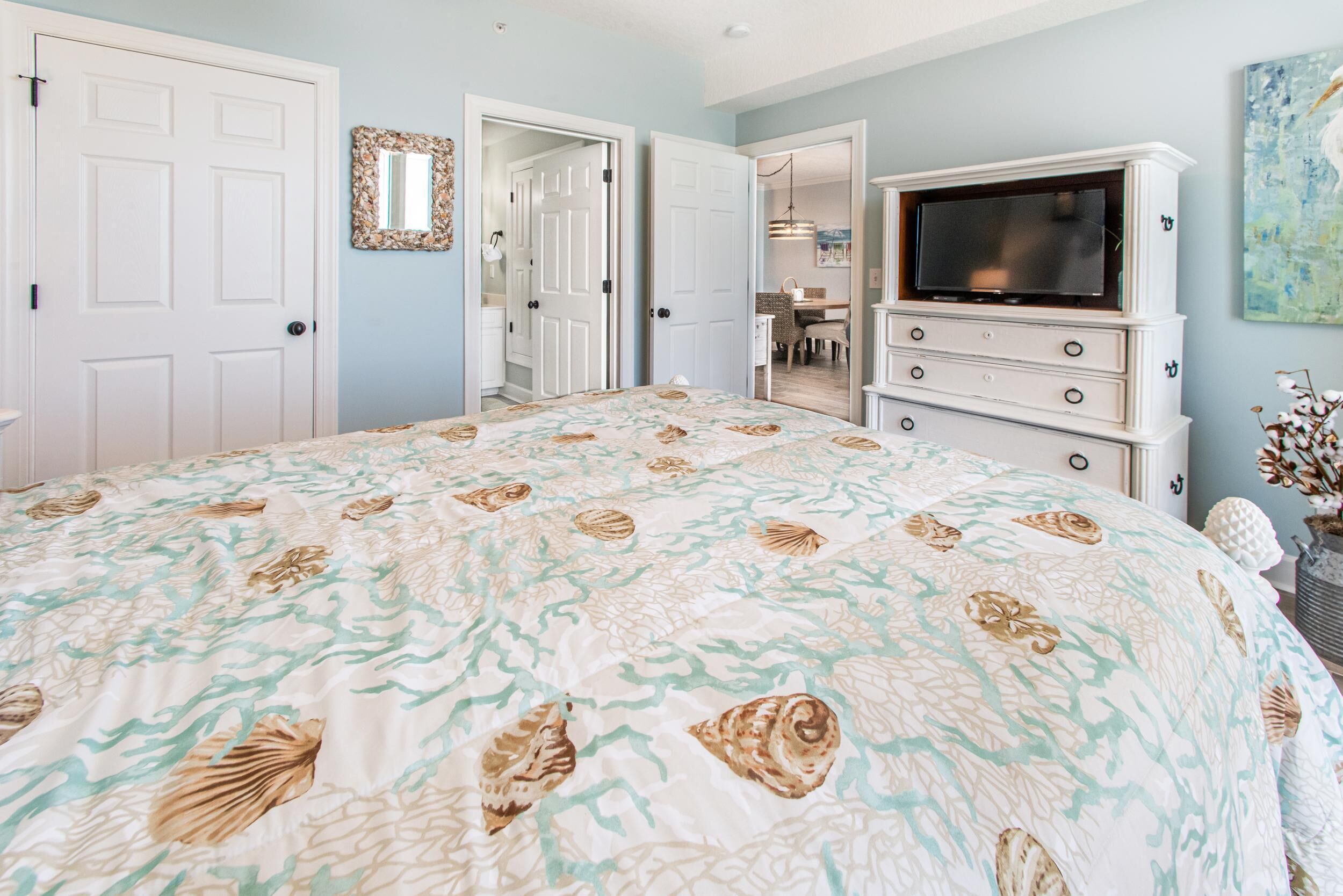 Een slaapkamer met een bed, een dressoir, een televisie en een deur die naar een andere kamer leidt.