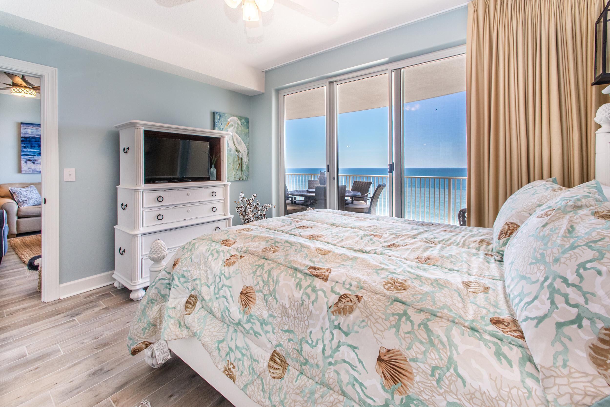Un dormitorio con una cama grande, un aparador, un televisor y un balcón con vista al océano.